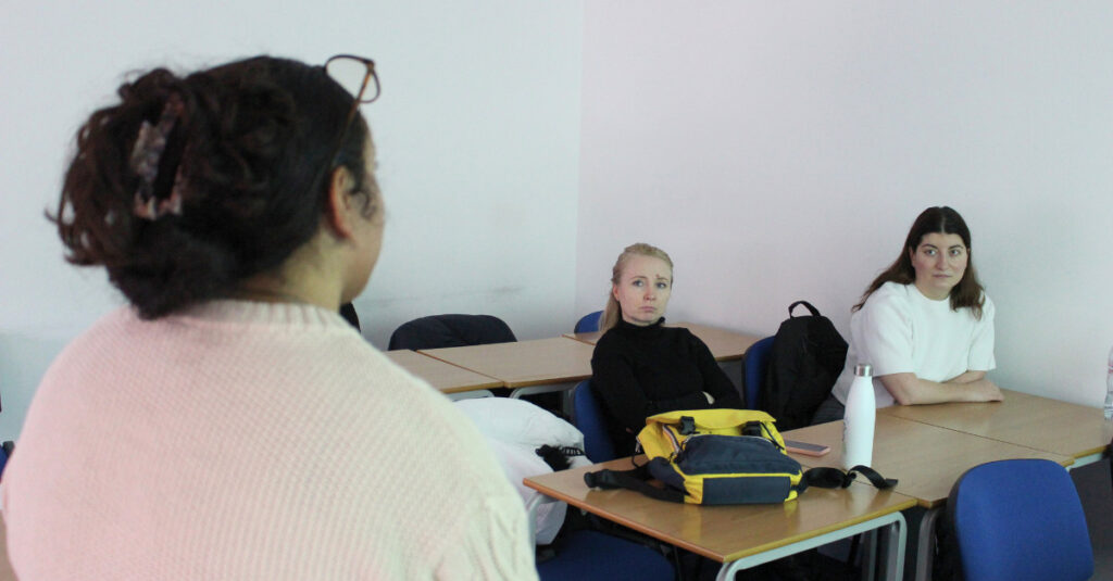 Two RCL BSc students sit in a classroom and listen to their tutor.